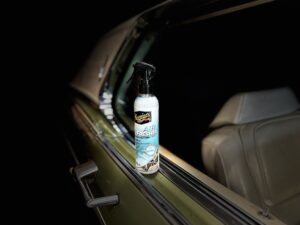Meguiar's Air Re-Fresher Odor Fighting Spray- New Car Scent staat op een deur rand van een auto